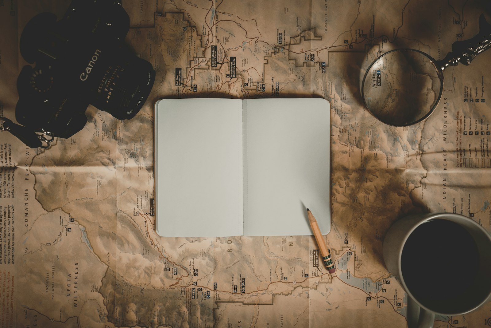 Open leather travel journal with a fountain pen, map and pressed flowers on a wooden table
