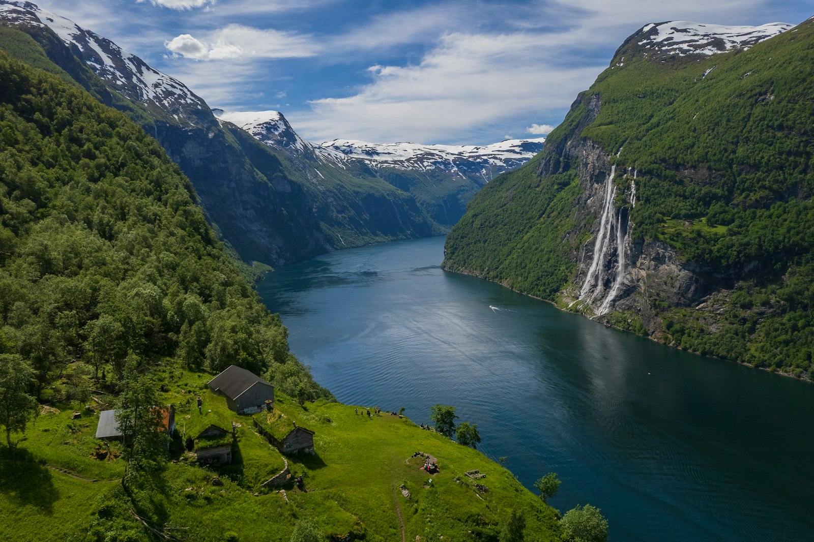 Steep green Norwegian fjord walls dropping to still dark water with a small village